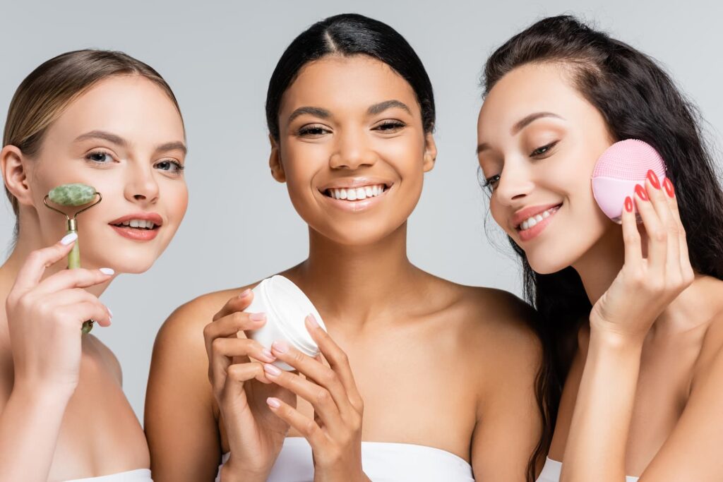 Glade multietniske kvinder der smiler og holder kosmetiske produkter